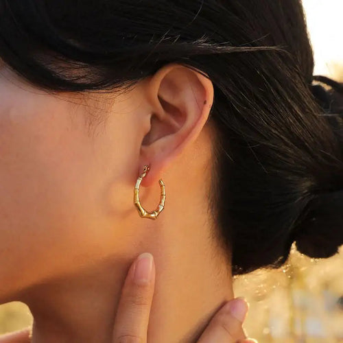 Close-up of an ear wearing a gold hoop earring with a blurred natural background